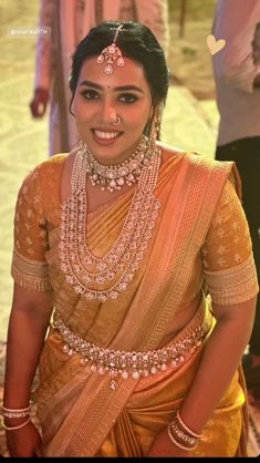 a woman in an orange and gold sari with jewelry on her neck, smiling at the camera