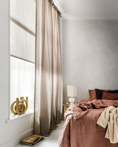 a bed sitting next to a window in a bedroom under a light brown blanket on top of a bed