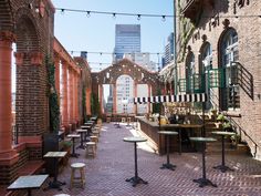 an outdoor seating area with tables and stools on the brick walkway between two buildings