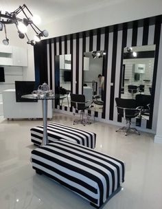 a salon with black and white striped chairs, mirrors and lights on the wall behind them