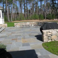 an outdoor patio with stone walls and seating area, surrounded by trees in the background