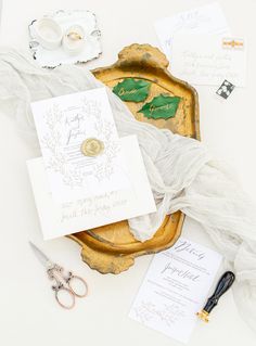 the wedding stationery is laid out on top of an antique tray with scissors and paper