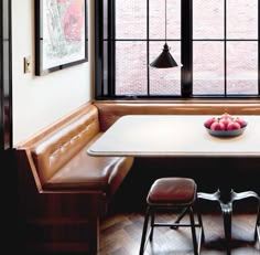 a corner table with two benches and a bowl of fruit on it in front of a window