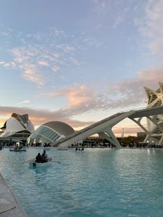 people are sitting in the water at sunset near an architecturally designed swimming pool and bridge