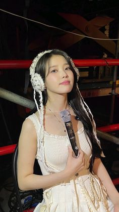 a woman in a white dress holding a microphone next to a boxing ring with red ropes