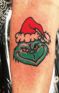 a green and red tattoo on the leg of a person wearing a santa claus hat