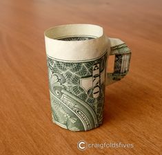 a cup made out of dollar bills sitting on top of a wooden table