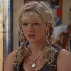 a woman with blonde hair wearing a necklace and looking at the camera while standing in front of a store