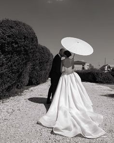 a bride and groom are standing under an umbrella in the middle of a gravel road