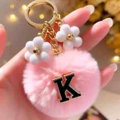 a pink keychain with white beads and a letter k on the front is held in someone's hand