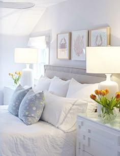 a white bed topped with lots of pillows next to two lamps and pictures on the wall