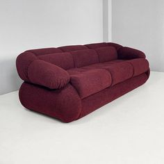 a large red couch sitting on top of a white floor next to a wall in an empty room