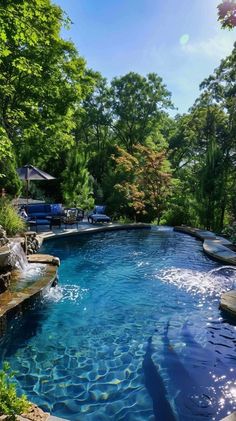 an outdoor swimming pool surrounded by lush green trees and water features blue skies, sun shining through the leaves