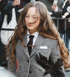 a woman with long hair wearing a suit and gloves on the street in front of a crowd