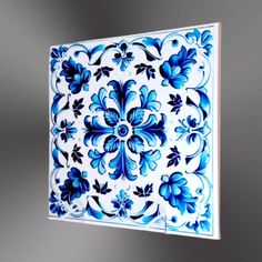 a blue and white square tile hanging on the wall with an intricate flower design in it