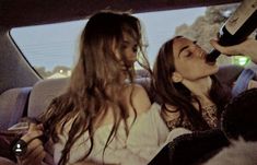 two women sitting in the back seat of a car and one is drinking from a bottle