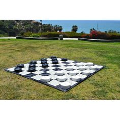 a giant checker board in the middle of a grassy area with water and trees in the background