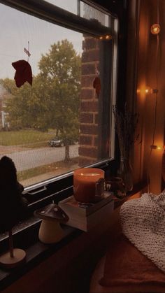 a candle is sitting on a window sill in front of an open window with fall leaves hanging from it