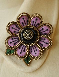 a purple flower brooch sitting on top of a white cloth