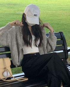 a woman sitting on top of a bench wearing a white hat and black pants with her hands behind her head