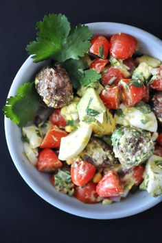 a bowl filled with meatballs, tomatoes and avocado garnished with cilantro