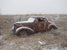 an old rusted out car sitting in the middle of a field covered in snow