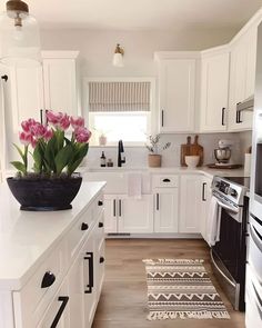 a kitchen with white cabinets and wooden floors has pink flowers in a black bowl on the counter