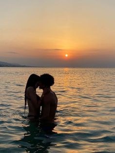 two people are kissing in the water at sunset