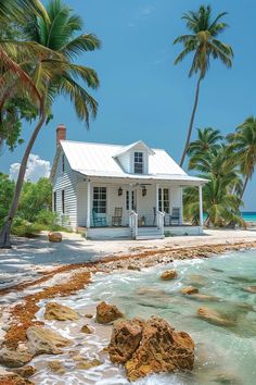 a white house sitting on top of a sandy beach next to the ocean with palm trees