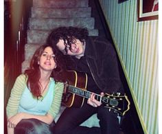 a man and woman are sitting on the stairs with their guitar in front of them