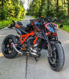 an orange and black motorcycle parked on the side of a road in front of trees