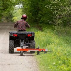 a man riding on the back of an atv down a dirt road next to trees