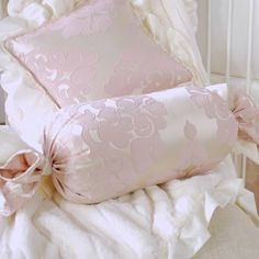 two pillows on top of a bed with ruffles and satin ribbon around the edges