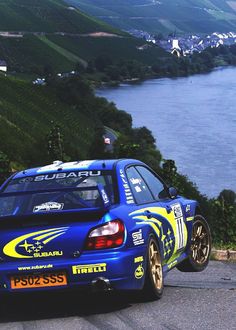 a blue car driving down a road next to a lake