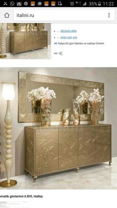 a gold dresser with vases and flowers on it in front of a large mirror