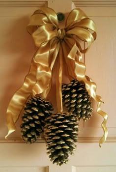 two pine cones hanging from a door with gold ribbons on the front and back of them