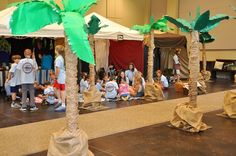 children are sitting on the floor in front of palm trees and tented tents with people standing around them