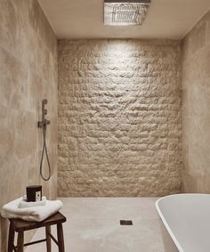 a white bath tub sitting next to a wooden stool in a room with stone walls