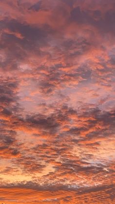 an airplane is flying in the sky at sunset with clouds and trees around it as the sun sets