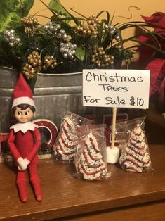 an elf is sitting next to some christmas trees and candy canes on a table