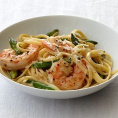 a bowl filled with pasta and shrimp on top of a white table cloth next to a fork