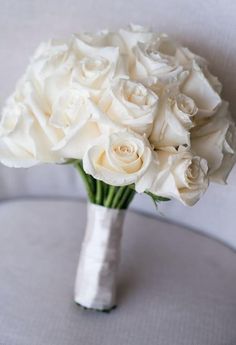 a bouquet of white roses sits in a vase on a round table with grey cloth