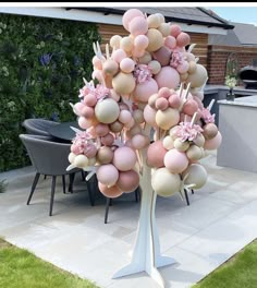 a tree made out of balloons and flowers in front of a patio table with chairs