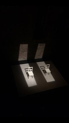 two white chairs sitting on top of a table in the middle of a dark room