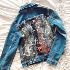 a jean jacket with flowers on it laying on top of a white bedding sheet