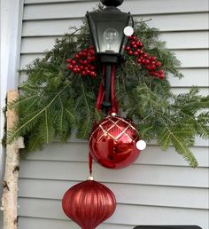 christmas decorations hanging from the side of a house with evergreen branches and red baubles