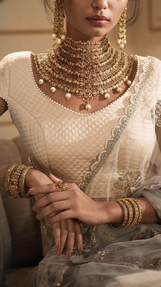 a woman in a white dress with gold jewelry on her neck and hands clasped together