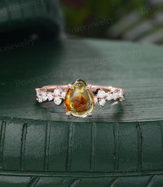 an orange and white diamond ring sitting on top of a green leather cushioned surface