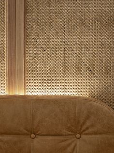 a brown leather couch sitting in front of a wall with wicker coverings on it