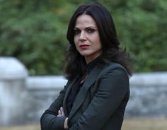 a woman standing with her arms crossed and looking at the camera while wearing a blazer